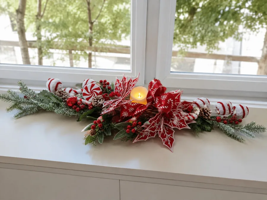 Centro de mesa natalino comprido com folhagem nevada, flores vermelhas e vela de LED acesa