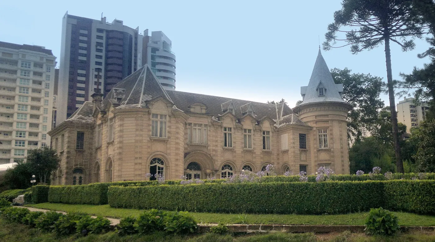 Castelo do Batel visto do jardim, com torres de telhado cônico e prédios altos ao fundo